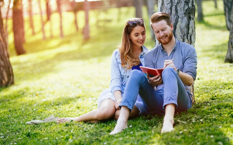 lifestyle image of a couple sitting beside a tree in an outdoors area